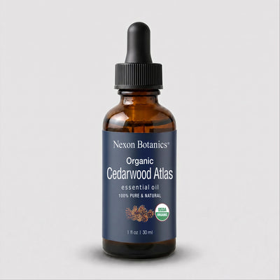 A 1 fl oz amber glass dropper bottle of Nexon Botanics Organic Cedarwood Atlas essential oil, featuring a dark blue label and black dropper cap, set against a light gray background.