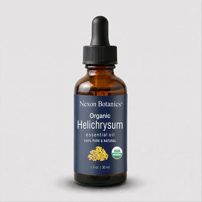 A 1 fl oz amber glass dropper bottle of Nexon Botanics Organic Helichrysum essential oil, featuring a dark blue label with white text and a black dropper cap, set against a light gray background.