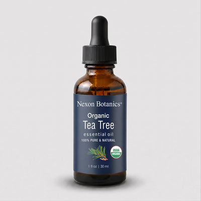A 1 fl oz amber glass dropper bottle of Nexon Botanics Organic Tea Tree essential oil, featuring a dark blue label with white text and a green USDA Organic seal, set against a light gray background.