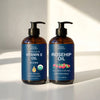 Two amber pump bottles of Newton Botanicals hair and skin oils standing side by side on a white surface with soft sunlight and shadows. The left bottle is labeled 'Organic Vitamin E Oil Blend' and the right bottle is labeled 'Rosehip Oil'.